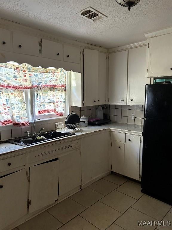 kitchen with white cabinets, sink, decorative backsplash, light tile patterned flooring, and black fridge