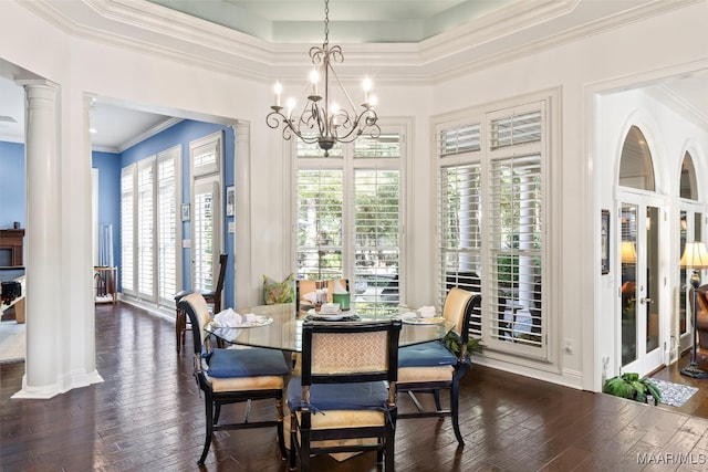 dining area with a raised ceiling, a notable chandelier, ornamental molding, dark wood-type flooring, and ornate columns