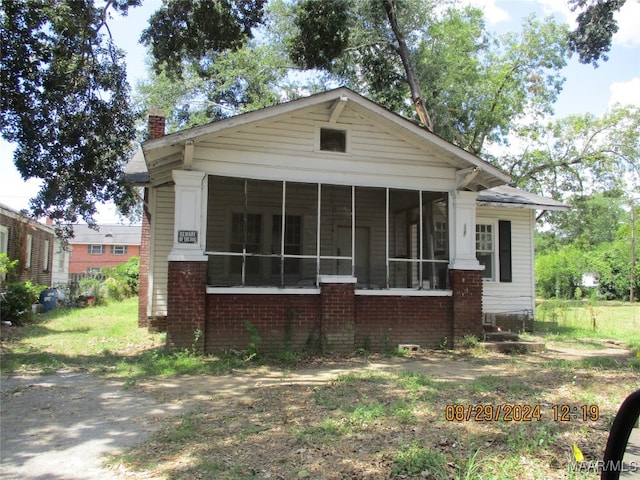 view of front of house featuring brick siding, a sunroom, and a chimney