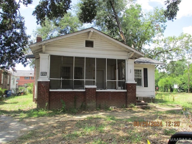 view of front of property featuring brick siding, a chimney, and a sunroom