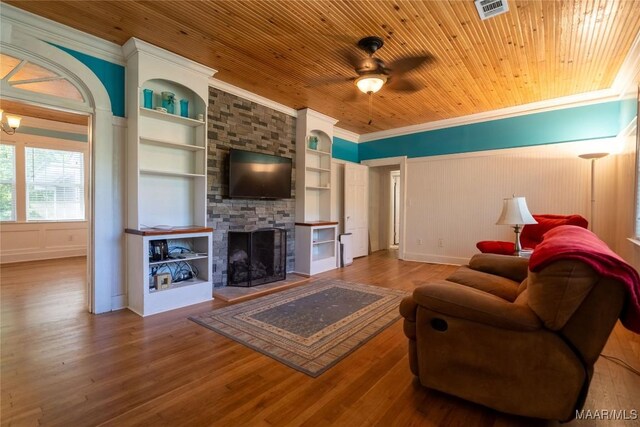 living room with hardwood / wood-style floors, wooden ceiling, built in features, a stone fireplace, and crown molding