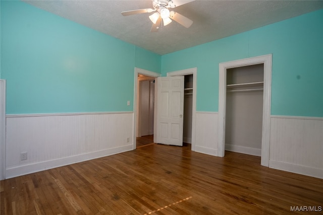 unfurnished bedroom with dark hardwood / wood-style flooring, two closets, a textured ceiling, and ceiling fan