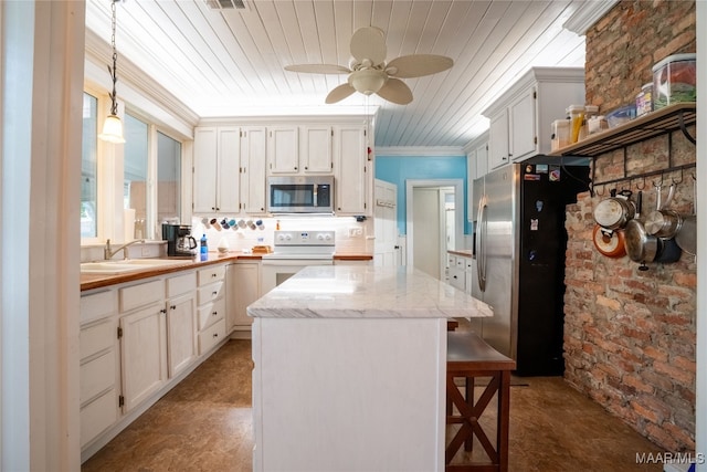 kitchen with hanging light fixtures, white cabinetry, sink, stainless steel appliances, and brick wall