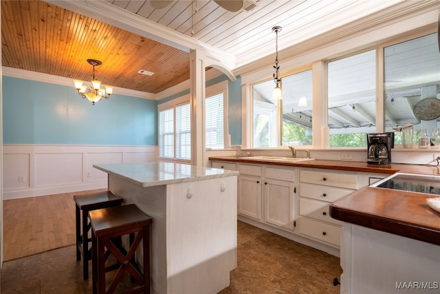 kitchen featuring white cabinets, a kitchen island, wooden ceiling, crown molding, and decorative light fixtures