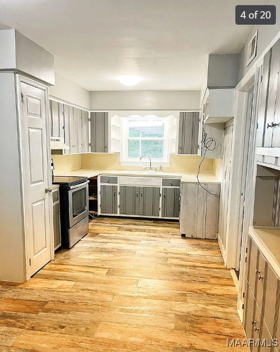 kitchen with custom exhaust hood, gray cabinetry, light wood-type flooring, and stainless steel range with electric stovetop