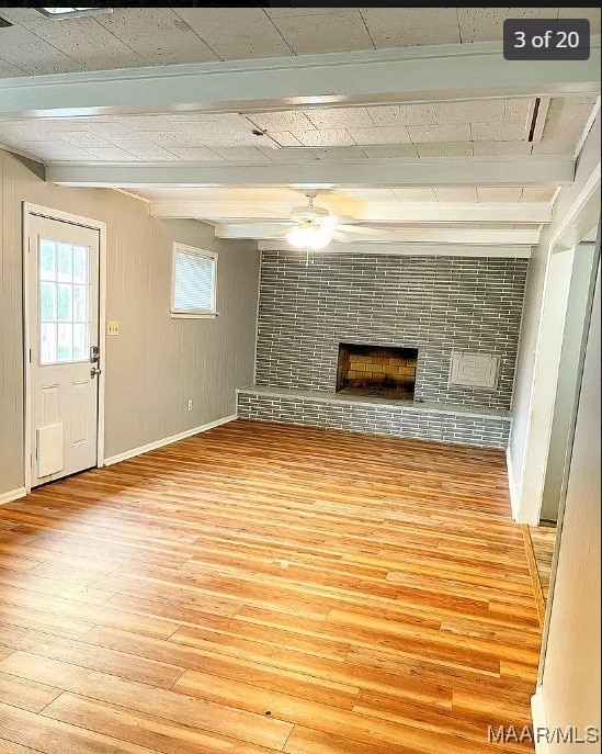 unfurnished living room with ceiling fan, beamed ceiling, hardwood / wood-style floors, and a brick fireplace