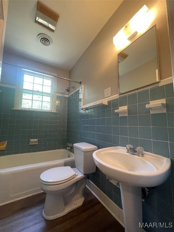 bathroom featuring tile walls, tiled shower / bath, and toilet