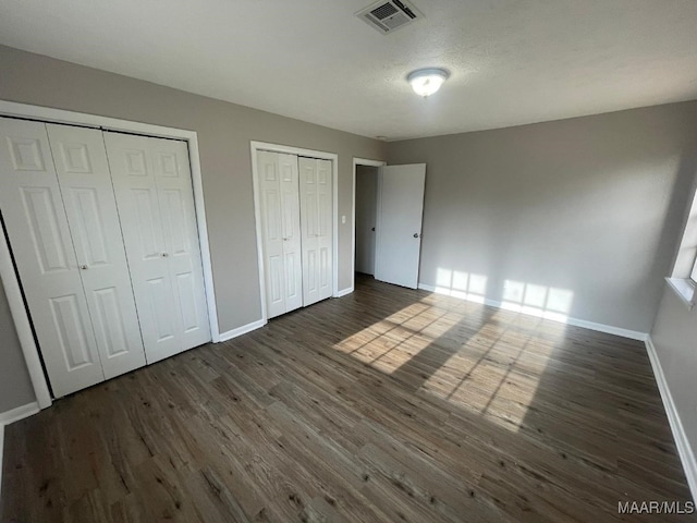 unfurnished bedroom featuring two closets, dark hardwood / wood-style floors, and a textured ceiling