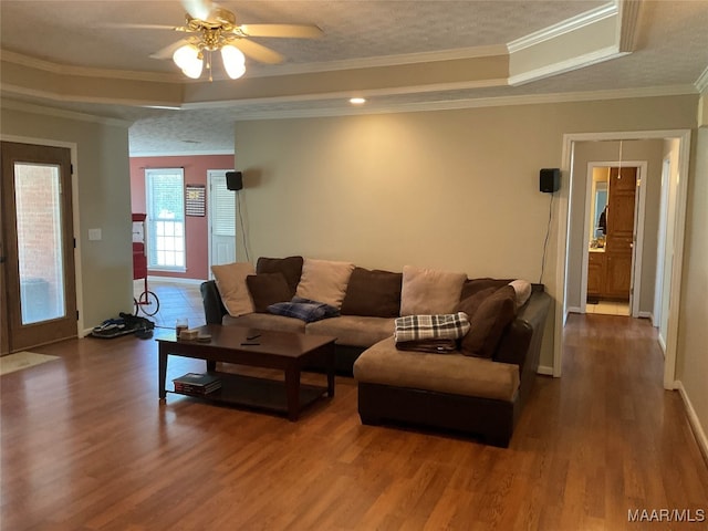 living room with ornamental molding, a textured ceiling, ceiling fan, a tray ceiling, and dark wood-type flooring