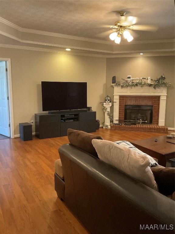 living room featuring a textured ceiling, a fireplace, ornamental molding, hardwood / wood-style flooring, and ceiling fan