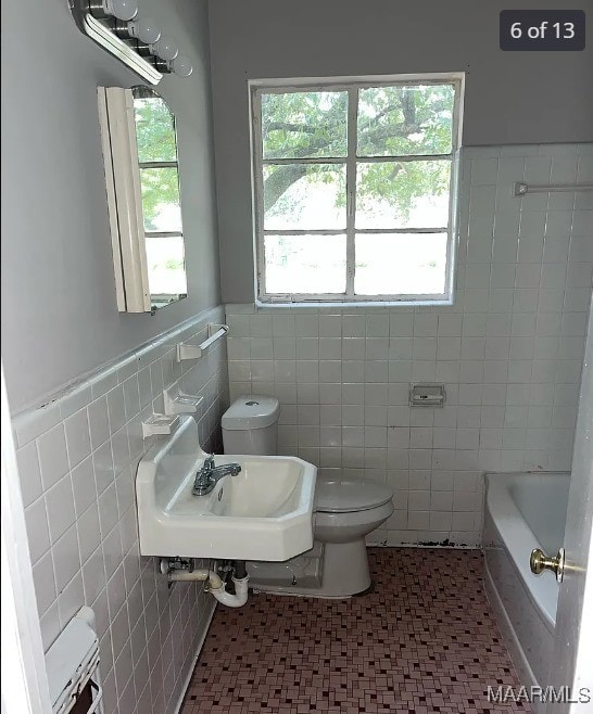 bathroom featuring a bathtub, plenty of natural light, toilet, and tile walls