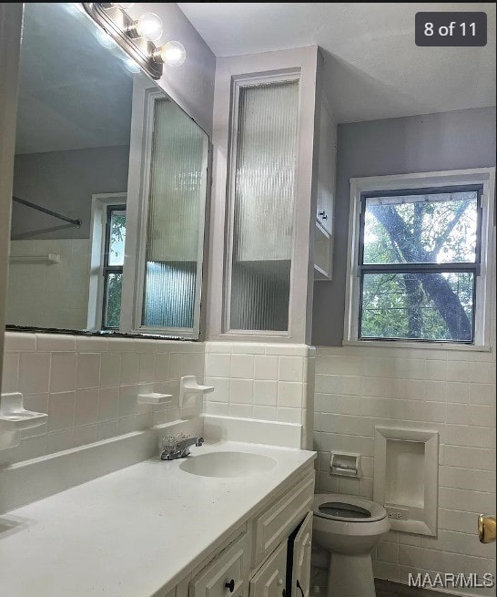 bathroom with tile walls, walk in shower, vanity, and toilet