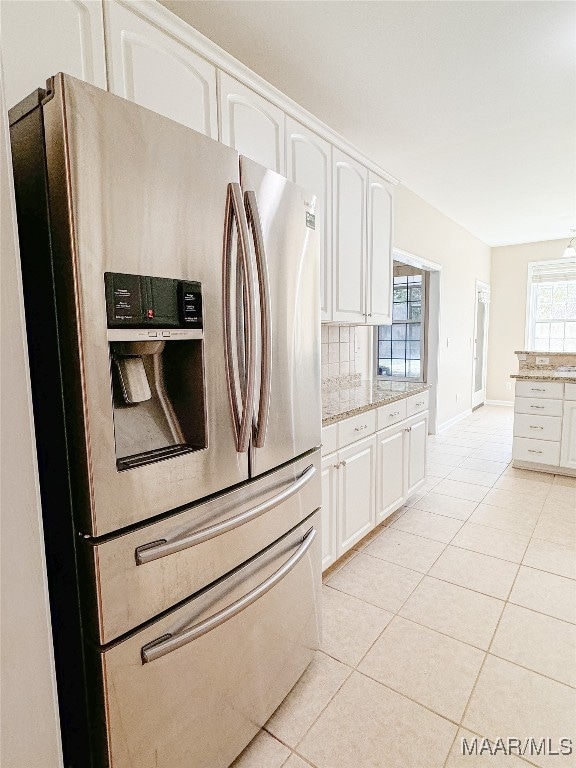 kitchen with stainless steel fridge, light stone countertops, white cabinets, and decorative backsplash