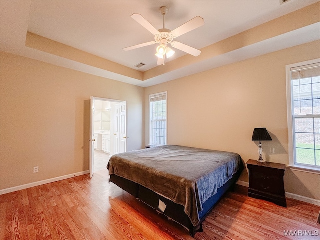 bedroom with a raised ceiling, wood-type flooring, ensuite bathroom, and ceiling fan