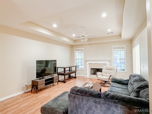 living room with light hardwood / wood-style flooring, a tray ceiling, ceiling fan, and a healthy amount of sunlight