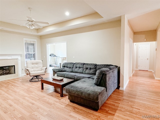 living room featuring a tray ceiling, ceiling fan, a tile fireplace, and light hardwood / wood-style flooring