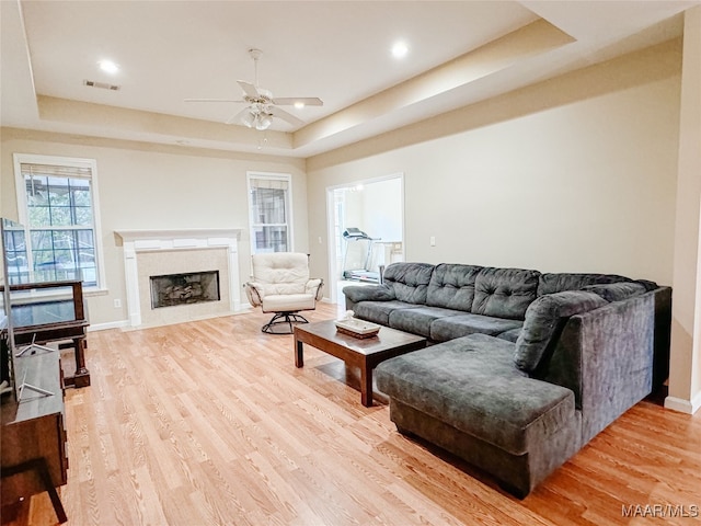 living room with a tray ceiling, wood-type flooring, a high end fireplace, and ceiling fan