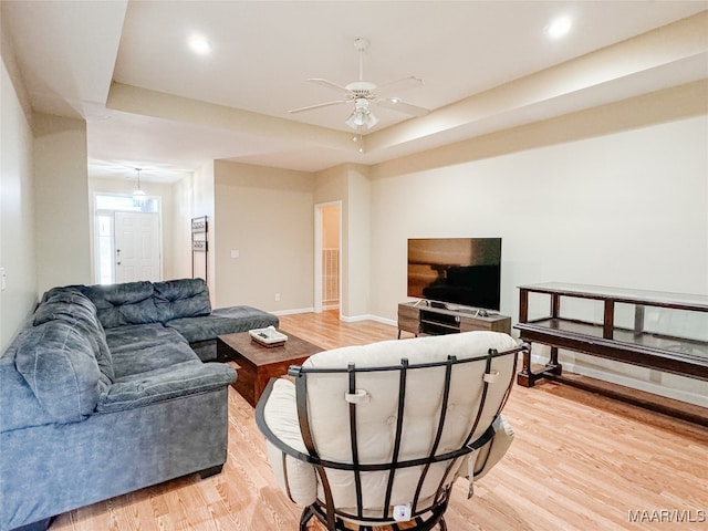 living room with a raised ceiling, ceiling fan, and light hardwood / wood-style floors