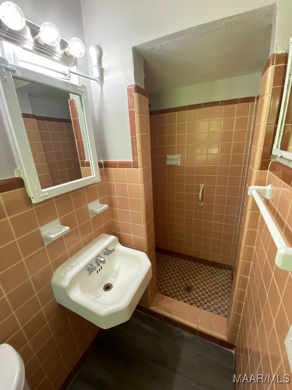 bathroom with tile walls, toilet, sink, and tiled shower