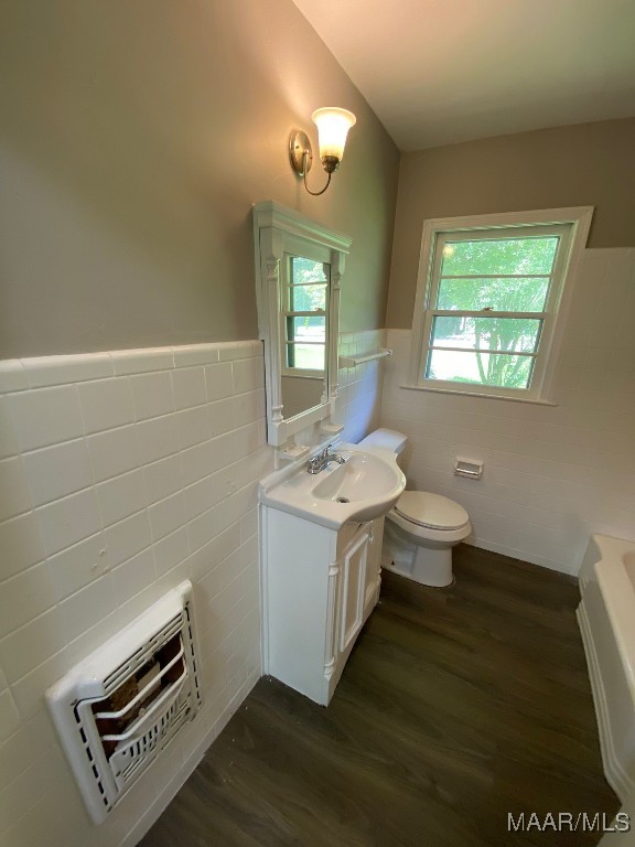 bathroom featuring tile walls, vanity, toilet, hardwood / wood-style flooring, and a washtub