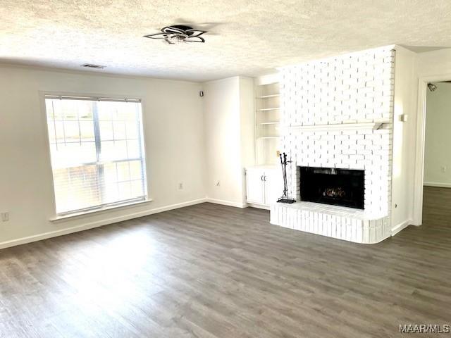 unfurnished living room with a textured ceiling, dark wood-type flooring, and a brick fireplace