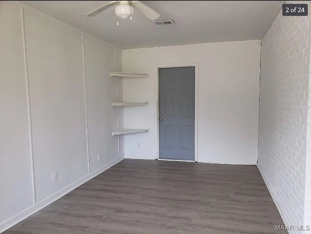 spare room featuring dark hardwood / wood-style flooring, ceiling fan, and brick wall