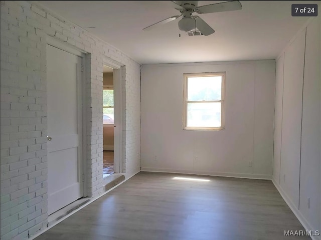 empty room with ceiling fan, hardwood / wood-style flooring, brick wall, and a healthy amount of sunlight