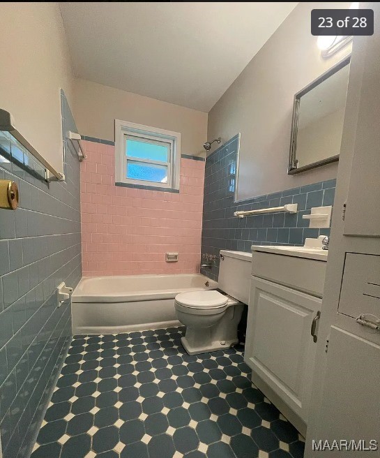 full bathroom with tile walls, tiled shower / bath, vanity, and toilet