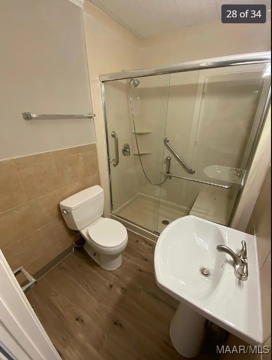 bathroom featuring tile walls, a shower with door, toilet, and wood-type flooring