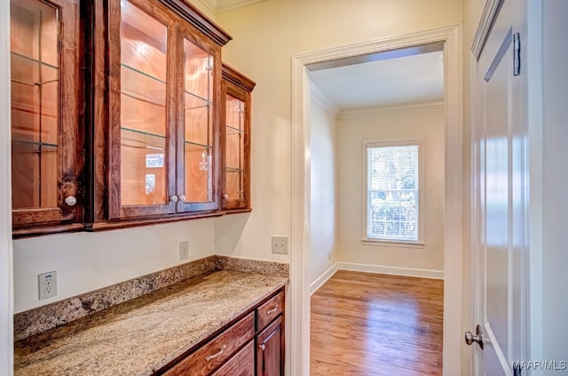 kitchen with light wood-type flooring, ornamental molding, and light stone countertops