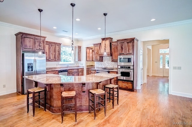 kitchen with light hardwood / wood-style flooring, light stone counters, a center island, hanging light fixtures, and appliances with stainless steel finishes