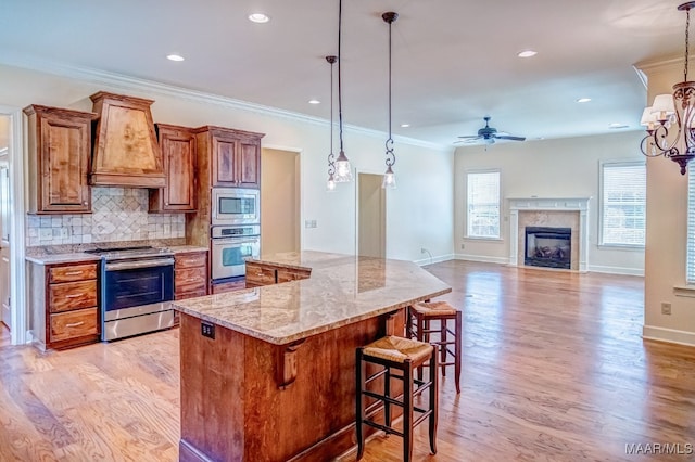 kitchen featuring decorative light fixtures, appliances with stainless steel finishes, premium range hood, and a high end fireplace