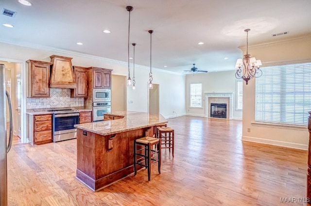 kitchen featuring a high end fireplace, custom range hood, ceiling fan with notable chandelier, stainless steel appliances, and a kitchen island