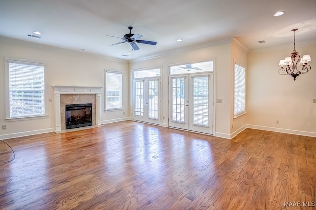 unfurnished living room featuring ceiling fan with notable chandelier, ornamental molding, a fireplace, and light hardwood / wood-style flooring