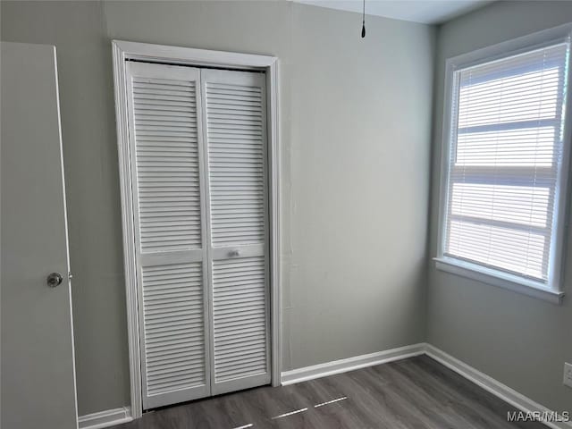 unfurnished bedroom with multiple windows, dark hardwood / wood-style flooring, and a closet