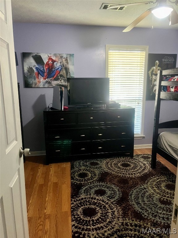 bedroom featuring multiple windows, ceiling fan, wood-type flooring, and a textured ceiling