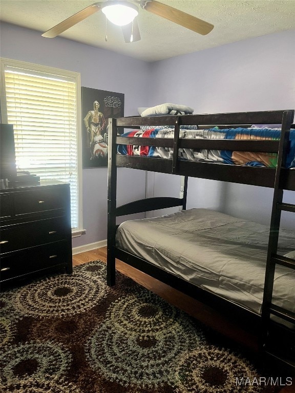 bedroom with hardwood / wood-style floors, ceiling fan, and a textured ceiling