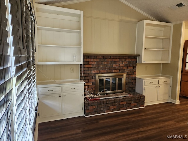 kitchen featuring dark wood-type flooring, lofted ceiling, crown molding, and a brick fireplace