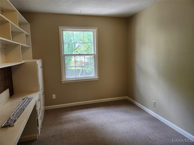 empty room featuring baseboards, dark colored carpet, and a textured ceiling