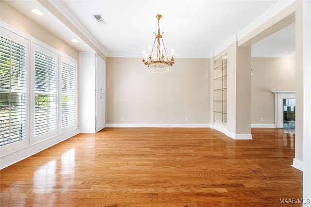 empty room featuring built in shelves, a chandelier, light hardwood / wood-style floors, and ornamental molding