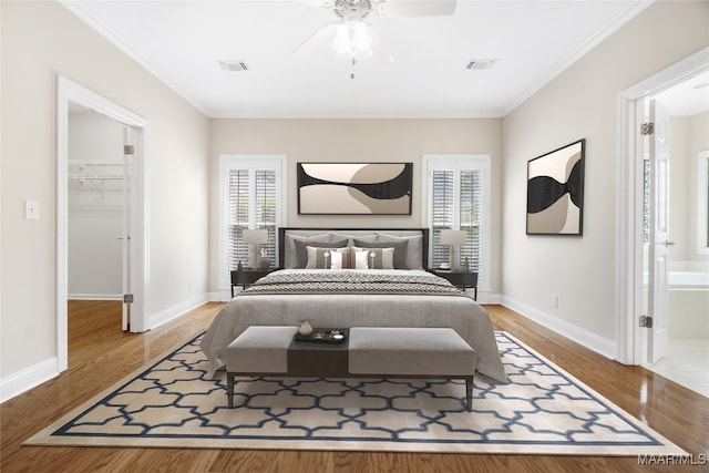 bedroom featuring crown molding, ensuite bath, wood-type flooring, ceiling fan, and a walk in closet