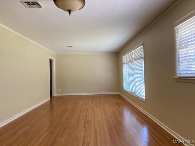 spare room featuring baseboards, wood finished floors, visible vents, and crown molding