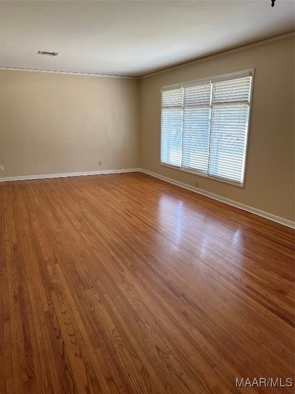 unfurnished room with baseboards, wood finished floors, and visible vents