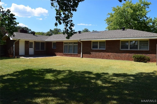 rear view of house with brick siding, a lawn, a chimney, and a patio