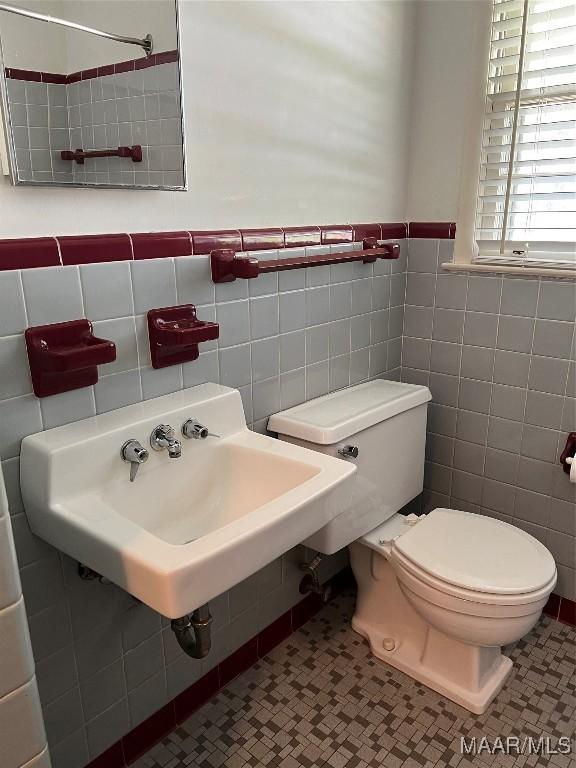 bathroom featuring tile walls, toilet, a wainscoted wall, and a sink