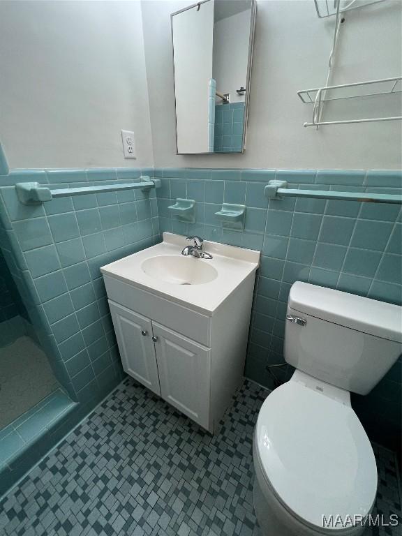 bathroom with wainscoting, vanity, tile walls, a shower, and toilet
