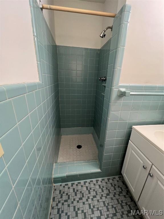bathroom featuring wainscoting, tiled shower, vanity, and tile walls
