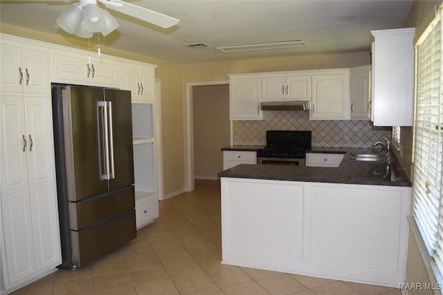 kitchen with under cabinet range hood, stainless steel appliances, dark countertops, a sink, and a peninsula