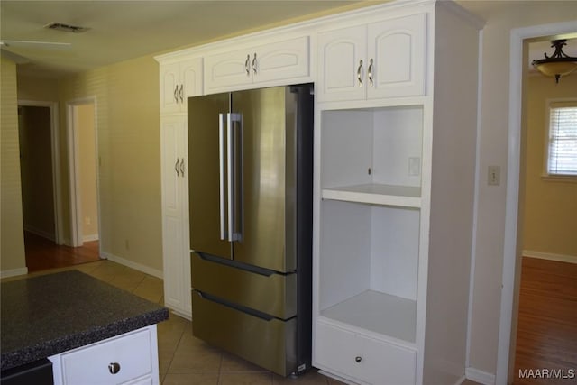 kitchen with light tile patterned floors, white cabinets, baseboards, visible vents, and freestanding refrigerator