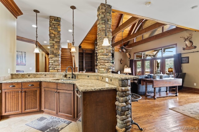 kitchen with decorative columns, light stone counters, open floor plan, hanging light fixtures, and a sink